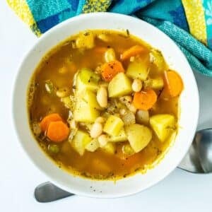 Bowl of soup with chunks of yellow potatoes, carrots, and white beans in it.