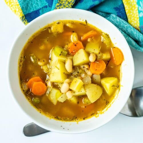 Bowl of soup with chunks of yellow potatoes, carrots, and white beans in it.