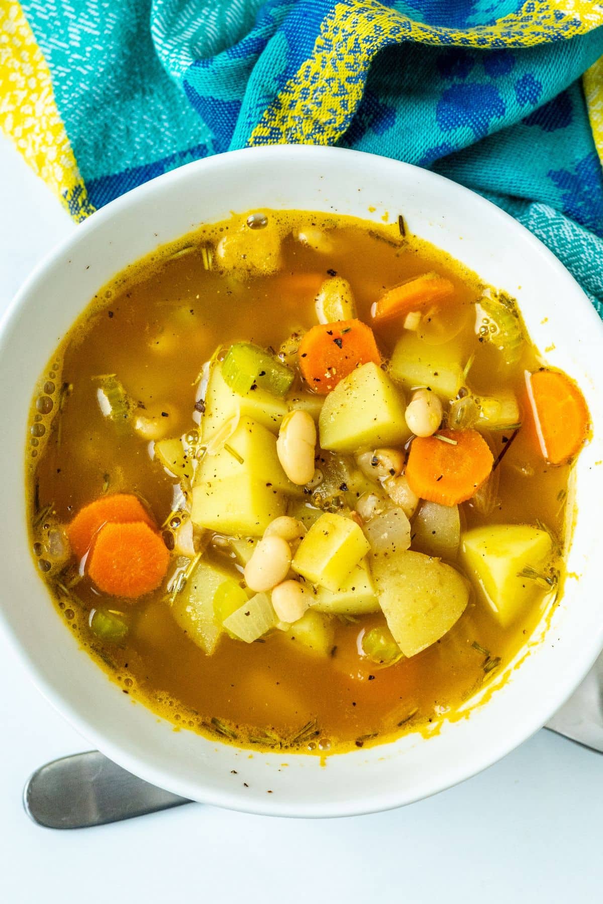 Bowl of soup made with diced potatoes, carrots, white beans, and dried rosemary.