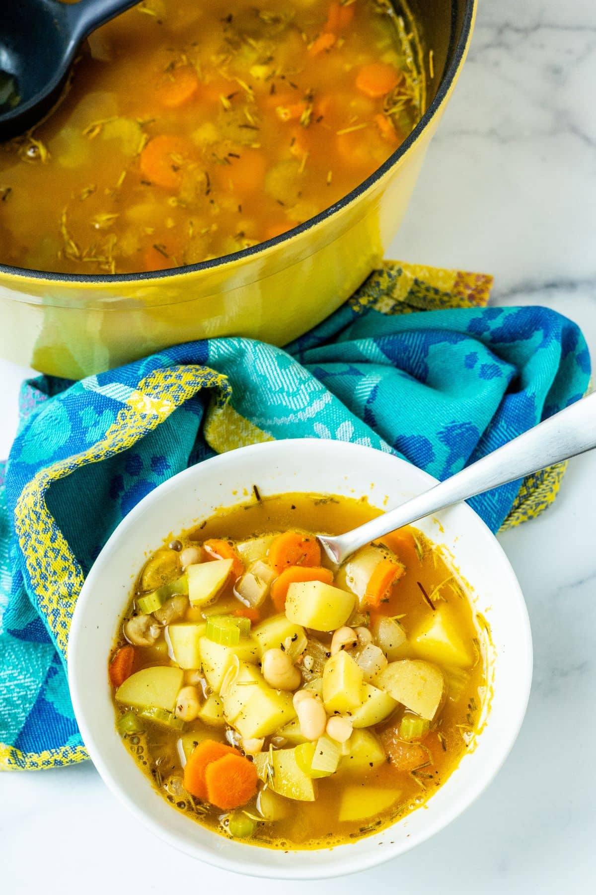 A pot of rosemary white bean potato soup and a bowl of soup with a spoon in it.