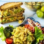 A green salad topped with tomatoes and chickpea salad and a chickpea salad sandwich, with text overlay: Curried Chickpea Salad.