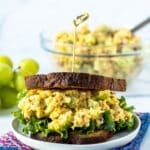 Chickpea salad sandwich and bowl of salad and bunch of green grapes in the background, with text overlay: Curried Chickpea Salad.