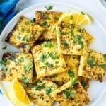 Platter of crispy tofu squares garnished with lemon wedges and fresh parsley, with text overlay: Lemon Pepper Tofu.