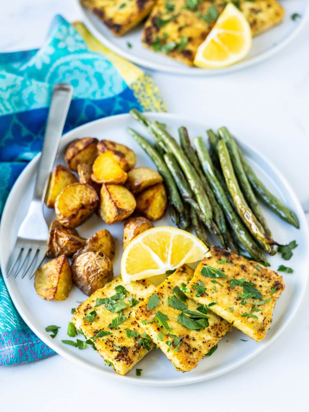 Lemon pepper tofu slices on a plate with roasted potatoes, green beans, and a lemon wedge.