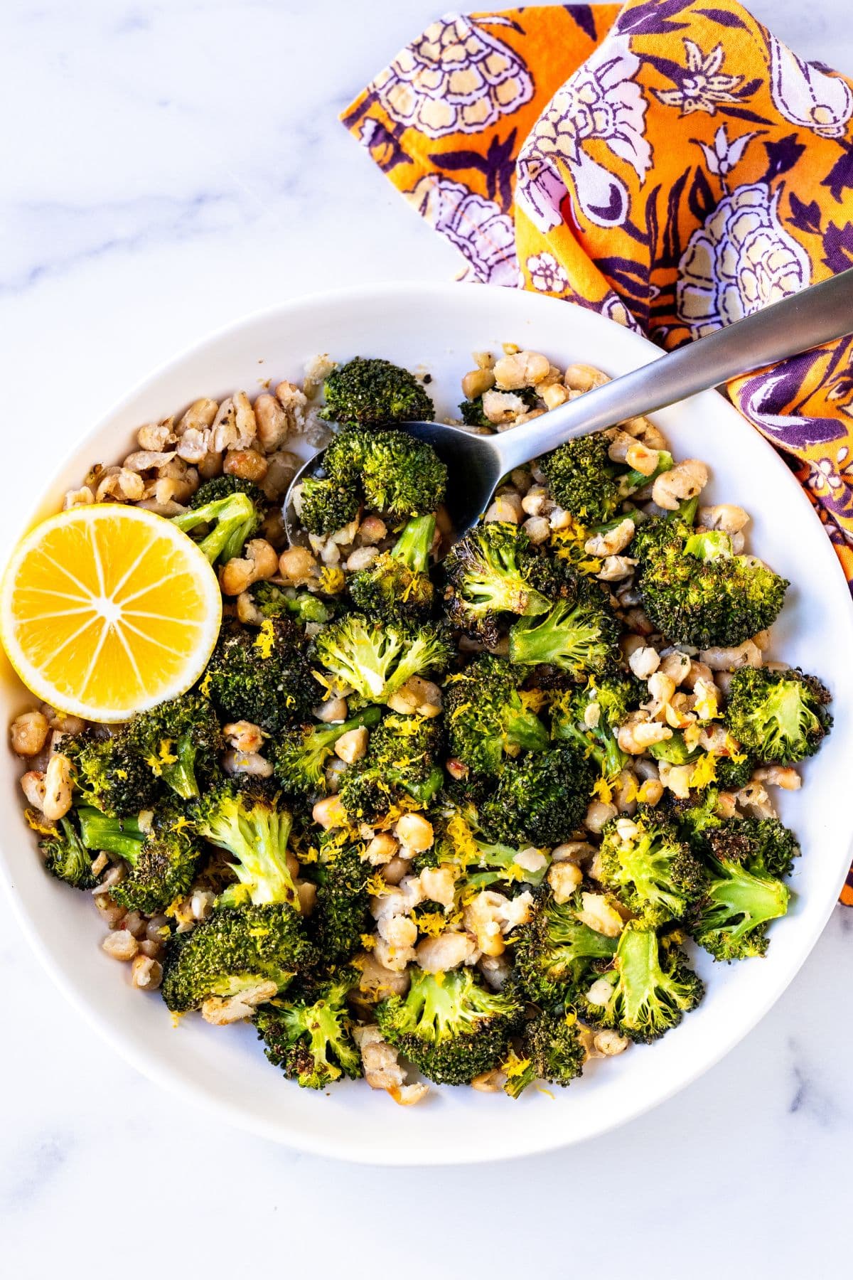 Roasted broccoli and white beans in a serving bowl garnished with lemon zest and a slice of lemon.