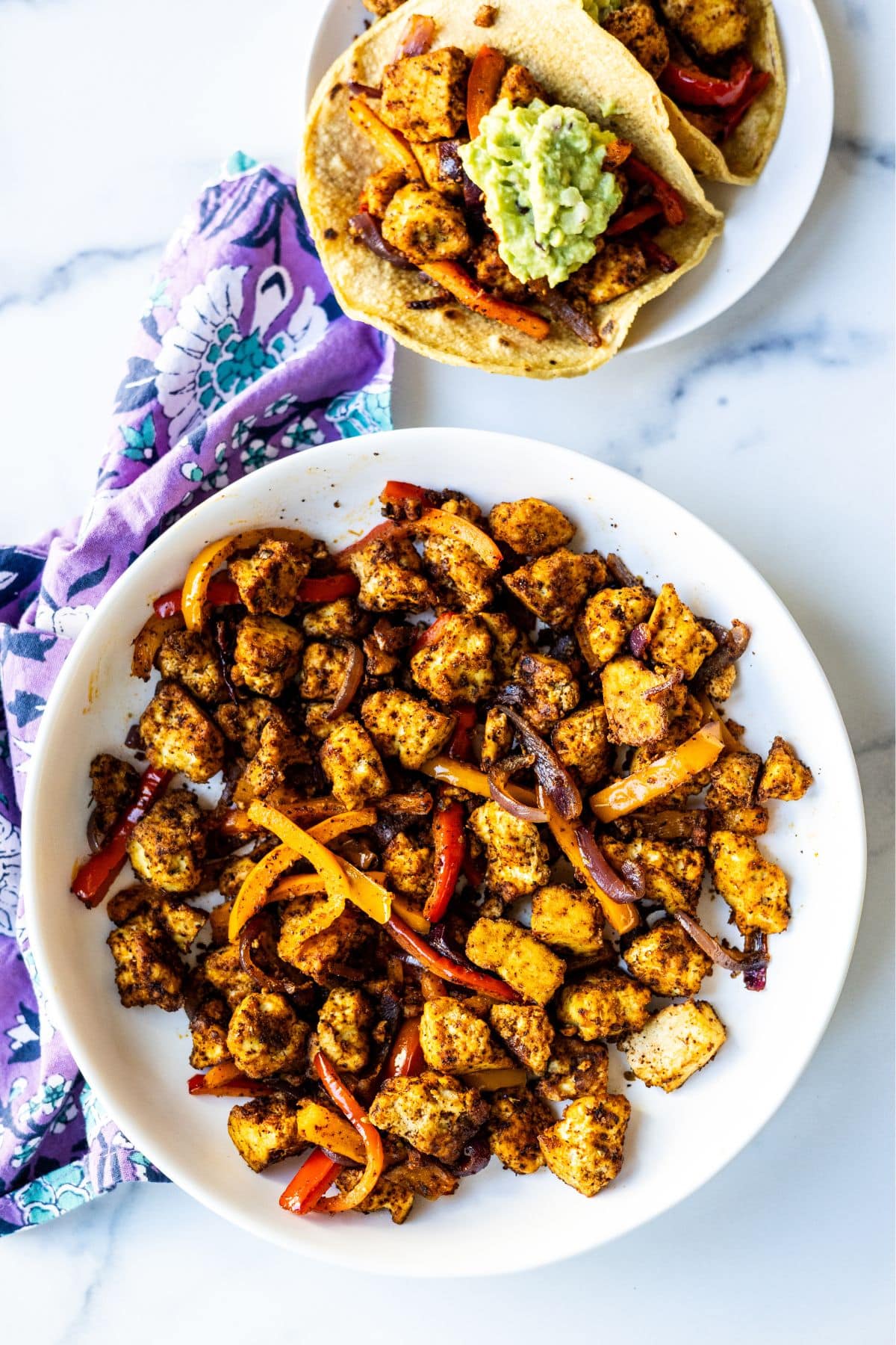 Tofu fajitas in a serving bowl and a plate with fajitas in corn tortillas topped with guacamole.
