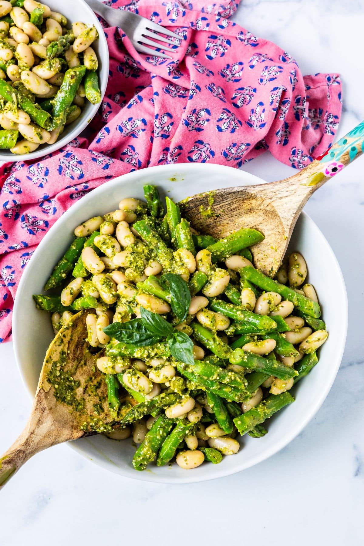 Serving bowl of white bean and asparagus salad with serving utensils.