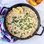 Chickpeas in a creamy sauce in a skillet, garnished with lemon wedges and fresh parsley, with a plate of sliced baguette on the side.