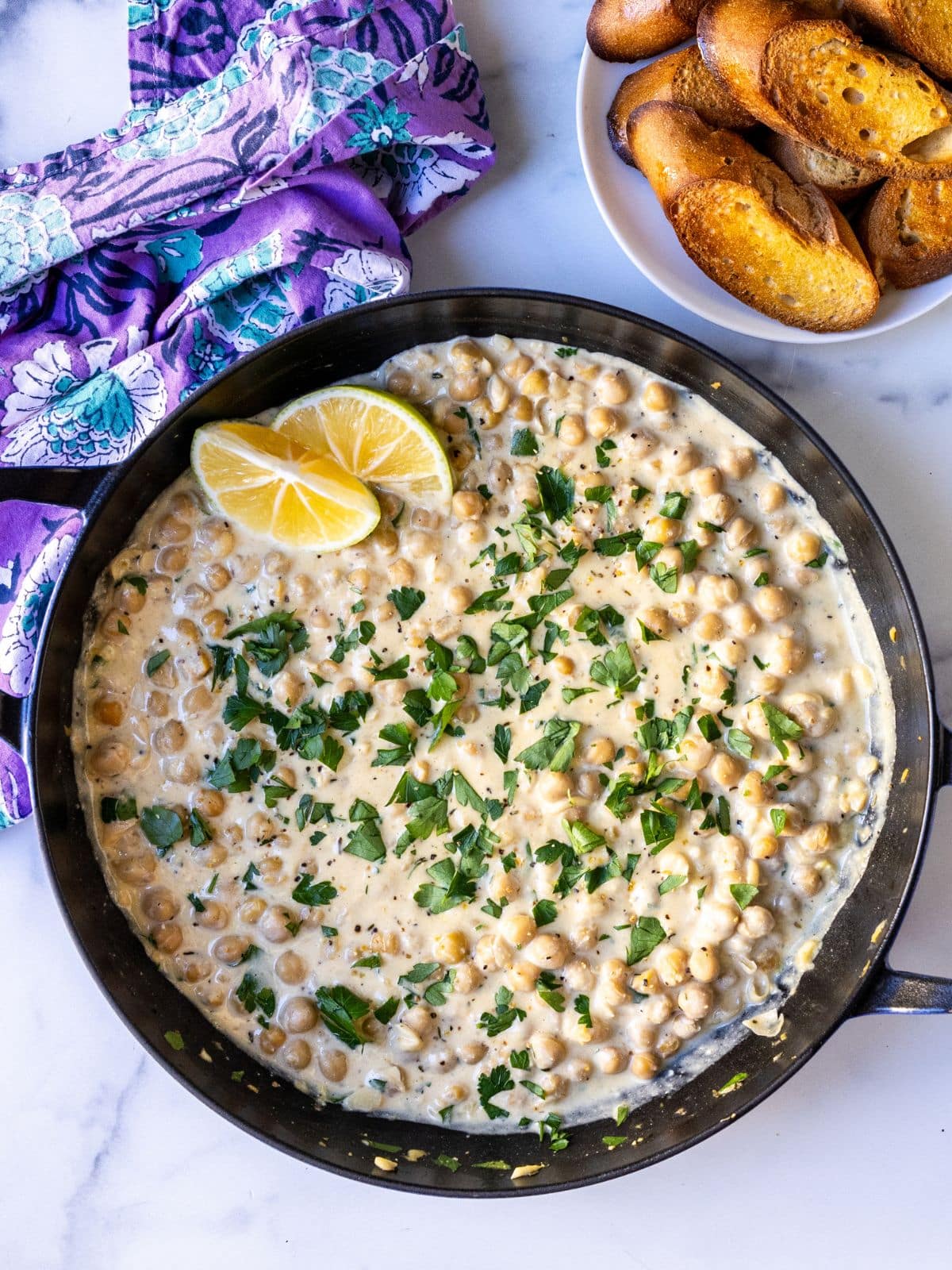Lemon pepper chickpea skillet with cashew cream and a plate of toasted baguette slices.