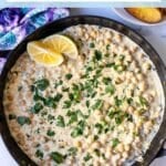 Chickpeas in a cashew cream sauce in a skillet, garnished with lemon wedges and fresh parsley, with text overlay: Lemon Pepper Chickpea Skillet.