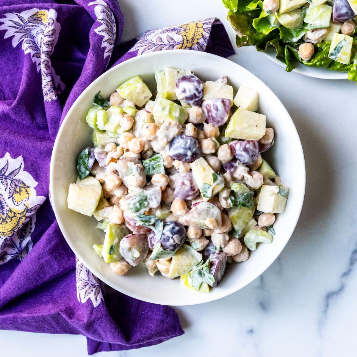 Bowl of chickpea Waldorf salad with a purple napkin alongside it.