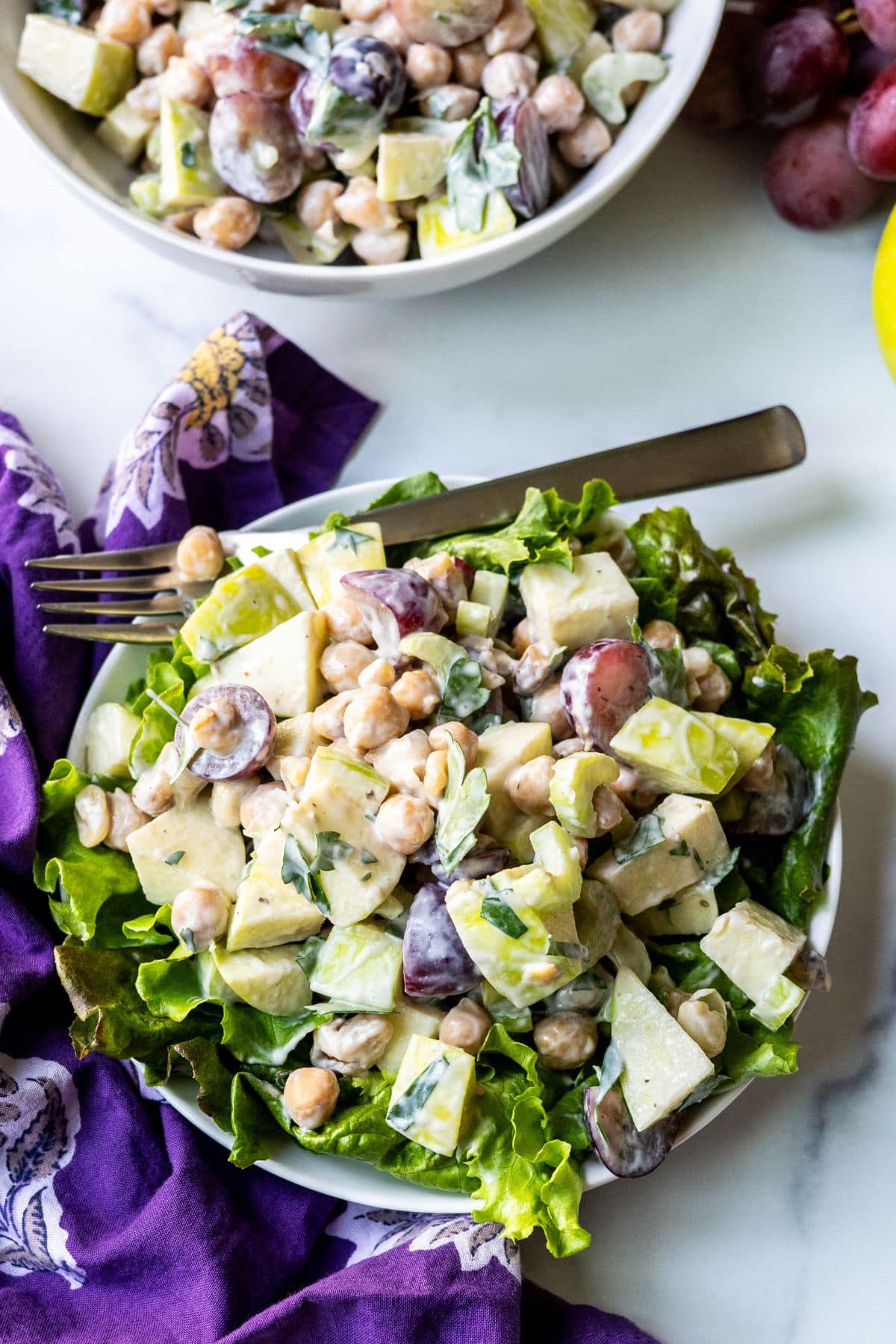 Chickpea Waldorf salad on a plate with mixed greens and a fork.