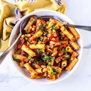 Bowl of rigatoni tossed in a white bean tomato sauce with Kalamata olives and garnished with fresh parsley.