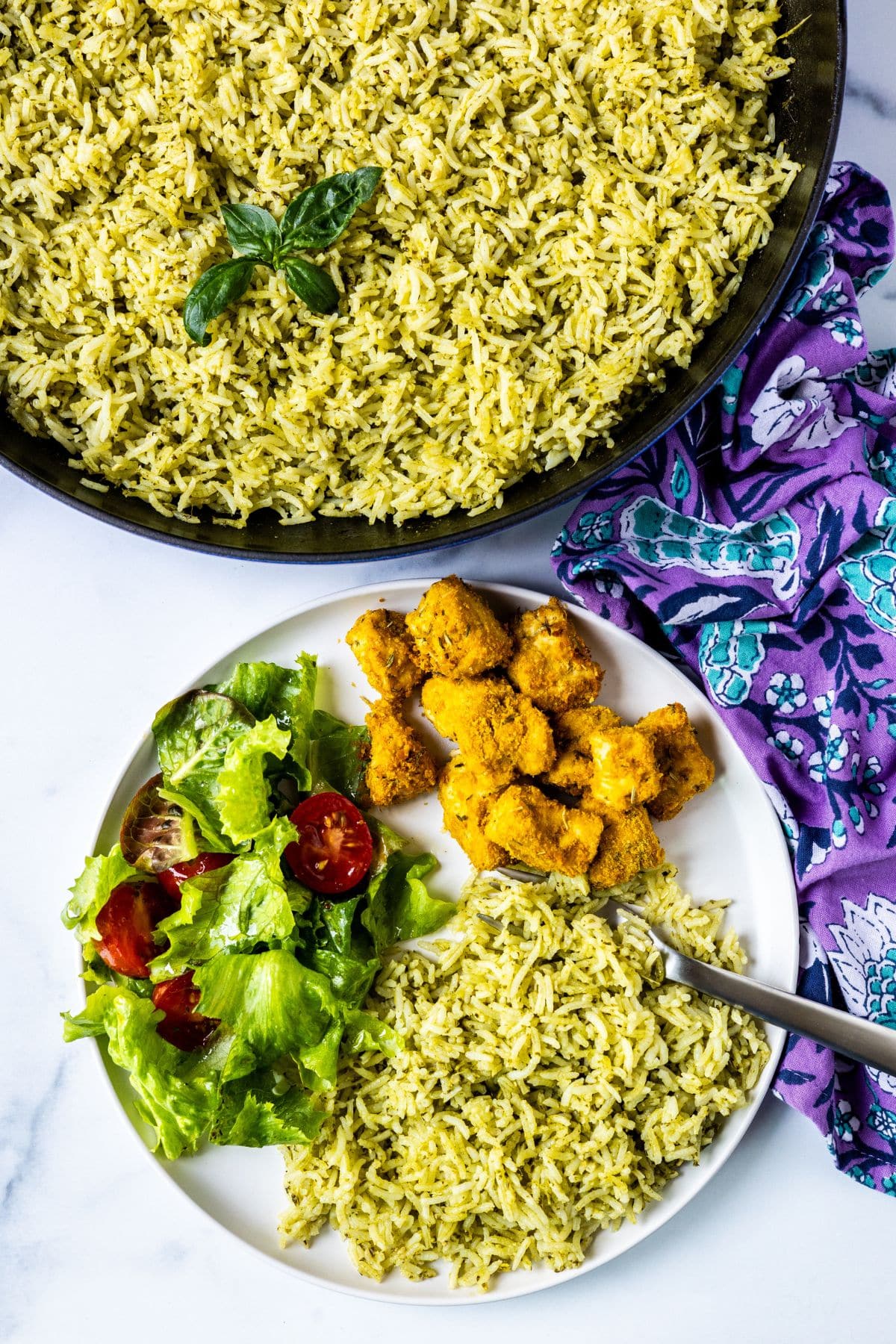 Dinner plate with pesto rice, salad, and tofu next to a skillet of baked pesto basmati rice.