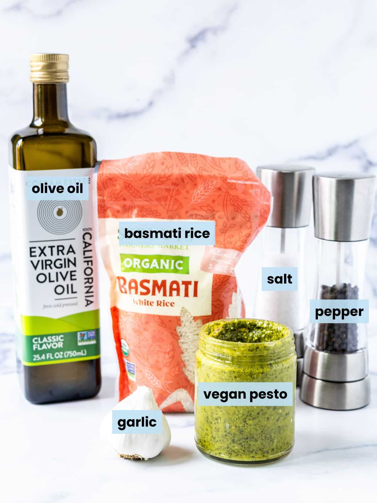 Garlic, a jar of vegan pesto, a bottle of olive oil, a bag of basmati rice, and salt and pepper grinders on a kitchen counter.