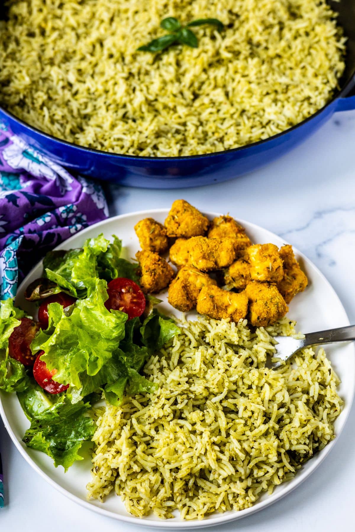 Pesto rice on a dinner plate with a green salad and baked rosemary tofu.