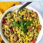 Bowl of vegan pesto quinoa salad with tomatoes, corn, and red onions, garnished with a sprig of fresh basil, with text overlay: Vegan Pesto Quinoa Salad with Corn and Tomatoes.