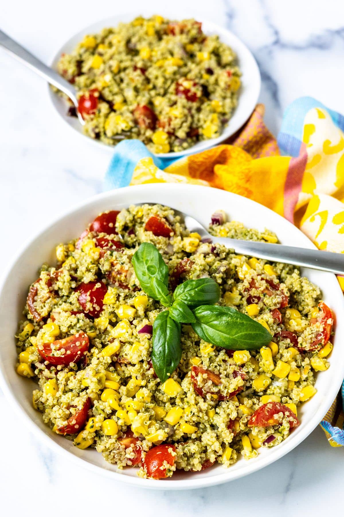 A serving bowl of pesto quinoa salad with an individual serving behind it.
