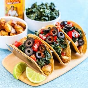 Three potato and kale tacos, bowls of roasted potatoes and massaged kale, and a bottle of hot sauce.