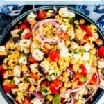 Bowl of orzo salad with tomatoes, vegan feta, and olives, with text overlay: Vegan Mediterranean Orzo Salad with Chickpeas.