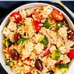 Bowl of millet salad with tomatoes, cucumbers, red onion, olives, and feta, with text overlay: Greek Millet Salad with Vegan Feta.