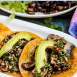 Tacos filled with sauteed mushrooms topped with chimichurri sauce and avocado slices, with text overlay: Vegan Mushroom Tacos with Chimichurri Sauce.