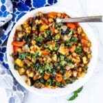 Spoon in a bowl of roasted chickpea ratatouille garnished with fresh basil.