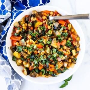 Spoon in a bowl of roasted chickpea ratatouille garnished with fresh basil.