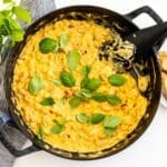Spoon in a skillet of creamy white beans with sun-dried tomatoes garnished with fresh basil leaves.