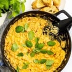 Spoon in a skillet of creamy white beans garnished with fresh basil leaves, with text overlay: Creamy White Bean Skillet with Sun-Dried Tomatoes.