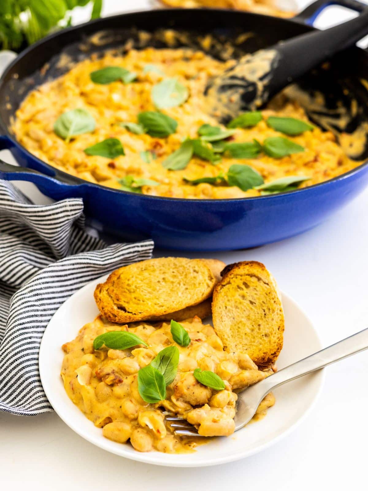 A plate of creamy white beans served with toasted slices of baguette with the skillet in the background.