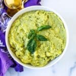 Bowl of pesto mashed potatoes garnished with fresh basil.