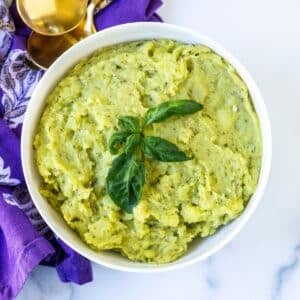 Bowl of pesto mashed potatoes garnished with fresh basil.