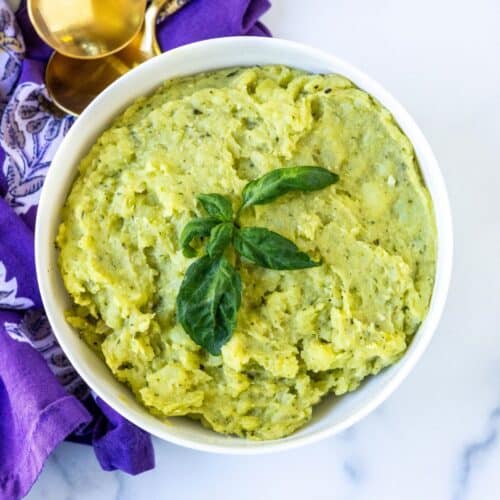 Bowl of pesto mashed potatoes garnished with fresh basil.