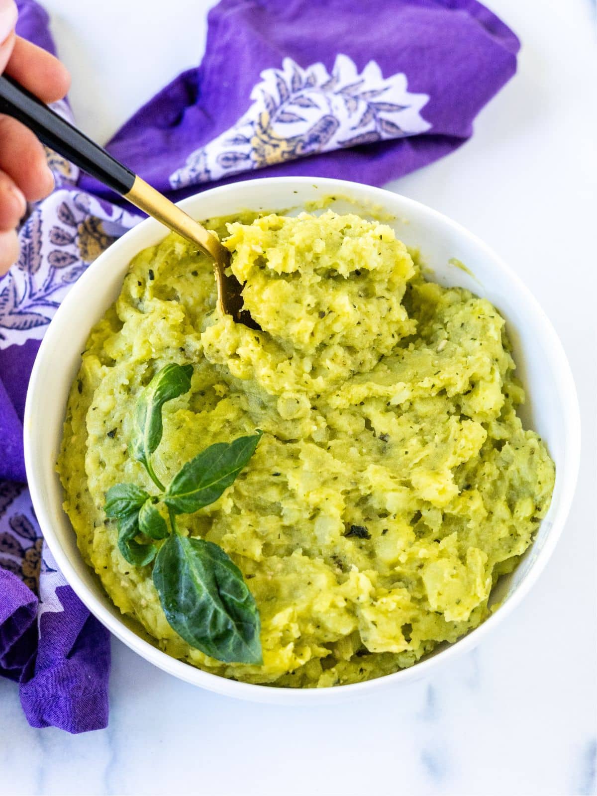Spoon in a bowl of pesto mashed potatoes garnished with sprig of basil.