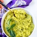 Spoon in a bowl of mashed potatoes garnished with fresh parsley, with text overlay: Vegan Pesto Mashed Potatoes.