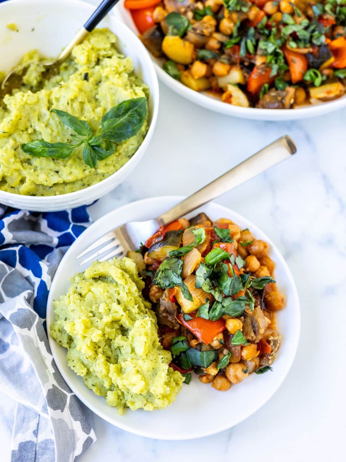 Pesto mashed potatoes and roasted chickpea ratatouille on a plate with serving bowls in the background.