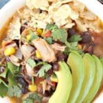 Bowl of soup topped with crushed tortilla chips, cilantro, and slices of avocado, with text overlay: Jackfruit Taco Soup with Black Beans and Corn.