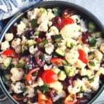 Bowl of raw cauliflower and vegetable salad, with text overlay: Mediterranean Cauliflower Salad.