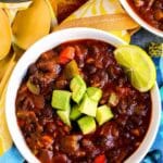 Bowl of black bean chili garnished with avocado and a slice of lime, with text overlay: 30-Minute Vegan Black Bean Chili.
