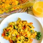 Serving of breakfast casserole on a plate next to a glass of orange juice and a casserole dish, with text overlay: Tofu Breakfast Casserole with Tater Tots.